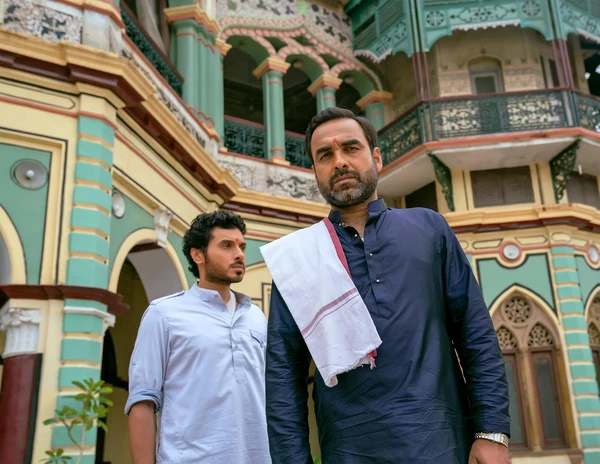 Two men stand in front of a colorful building in "Mirzapur".