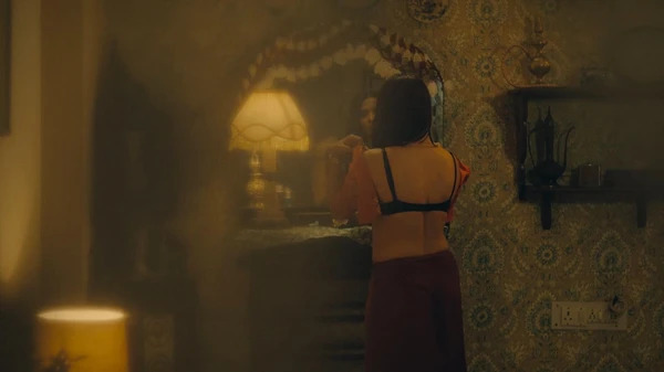 A woman in a bra standing by the mirror in Mandala Murders, with warm lighting in the room.（