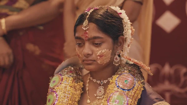 A girl in elaborate wedding attire looks somber in Ayali, hinting at village traditions.